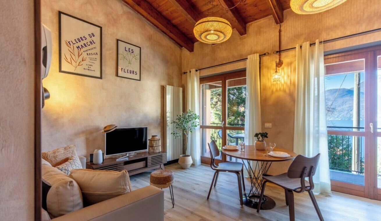 Un salon confortable avec un canapé, un téléviseur et une table à manger entourée de chaises. Des tableaux encadrés ornent le mur, et une grande fenêtre est agrémentée de rideaux.