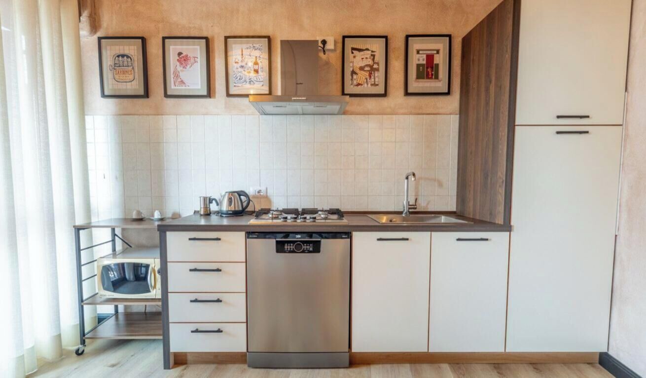 A modern kitchen with a dishwasher, stove, and microwave. There are framed pictures on the wall and a cabinet with drawers.