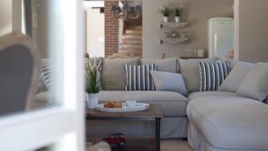 Ein Wohnzimmer mit einem Ecksofa, einem Couchtisch mit Korb und Pflanze, einem kleinen Tisch mit einem Spielzeugauto und einer Ziegelwand mit einem Kronleuchter.