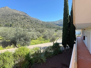 A balcony with a view of a mountainous landscape, olive trees, and a building with a tiled roof.