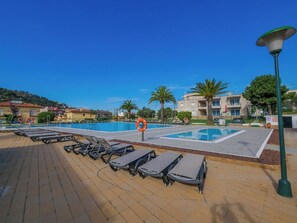 Un espace piscine avec des chaises longues et une bouée de sauvetage, entouré de bâtiments et de palmiers.