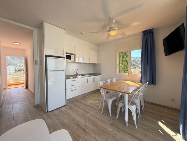 A modern kitchen with white cabinets, a microwave, and a dining area with a wooden table and white chairs.