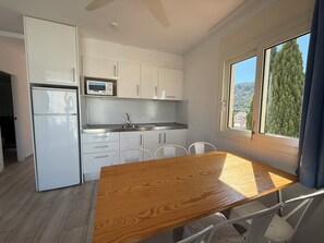 A compact kitchen with white cabinets, a microwave, a sink, and a dining area with a wooden table and chairs.