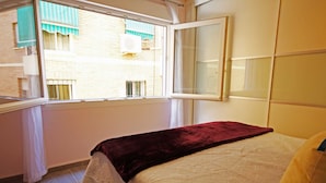 A bedroom with a bed, a window with blinds, and a view of buildings outside. - FLAT CENTER VIALIA STATIONS (MÁLAGA)