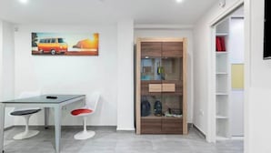 A modern room with a glass-top table, two chairs, a wooden wardrobe, and a shelf unit. - FLAT CENTER VIALIA STATIONS (MÁLAGA)