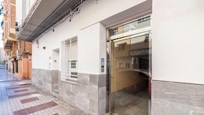 A building with a glass entrance, a tiled sidewalk, and a brick wall. - FLAT CENTER VIALIA STATIONS (MÁLAGA)