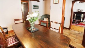 Un coin repas avec une table en bois, des chaises et un vase rempli de fleurs. On aperçoit une cheminée au fond.