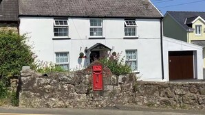 Un bâtiment blanc à deux étages, avec un mur de pierre à l’avant, une boîte aux lettres rouge et un garage sur le côté droit.
