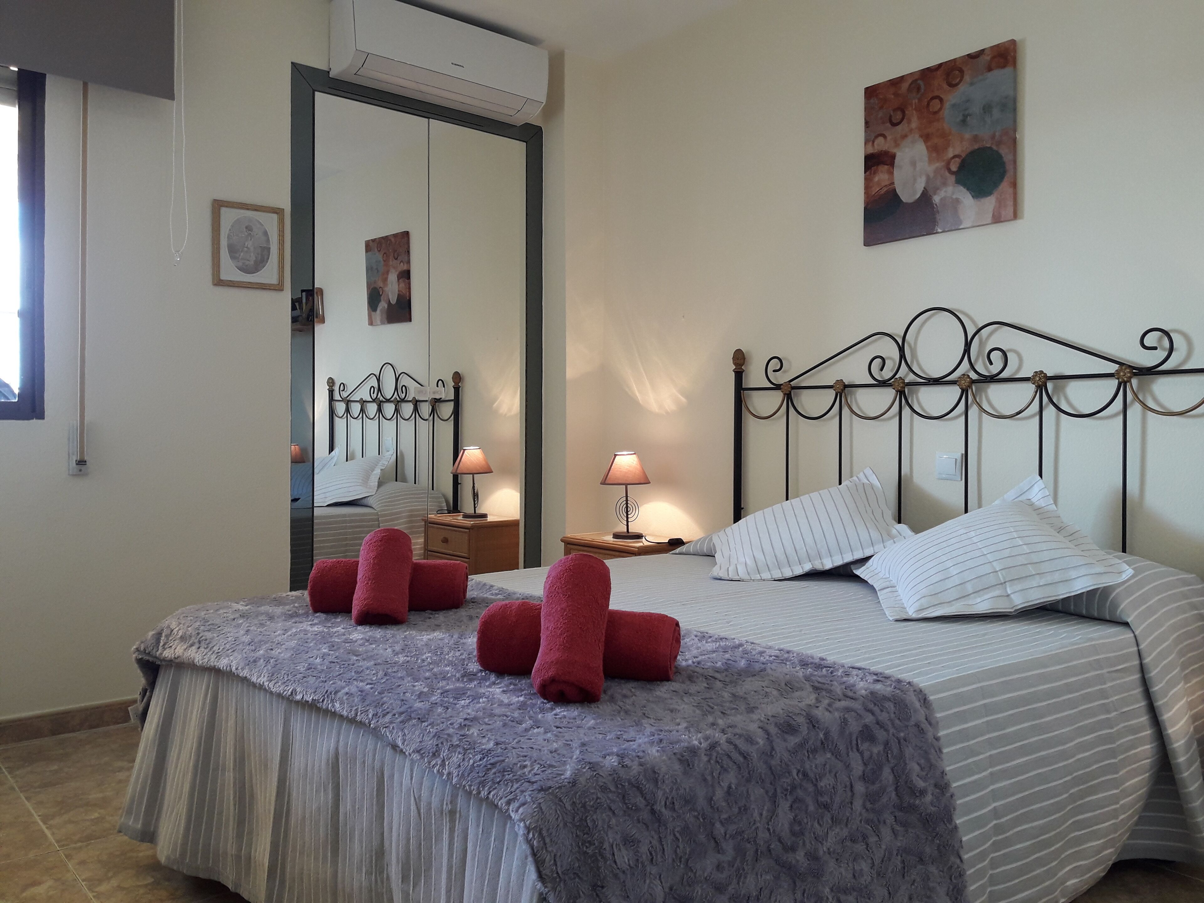 Une chambre à coucher bien rangée, avec un lit, deux tables de chevet, un miroir et un tableau accroché au mur.