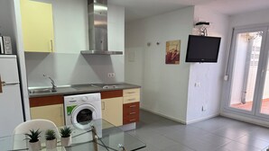 A modern kitchen with a built-in washing machine, a glass dining table with chairs, and a TV mounted on the wall. - Agi Peater Studio Apartamento for rent in Roses Girona. (Rosas / Roses)