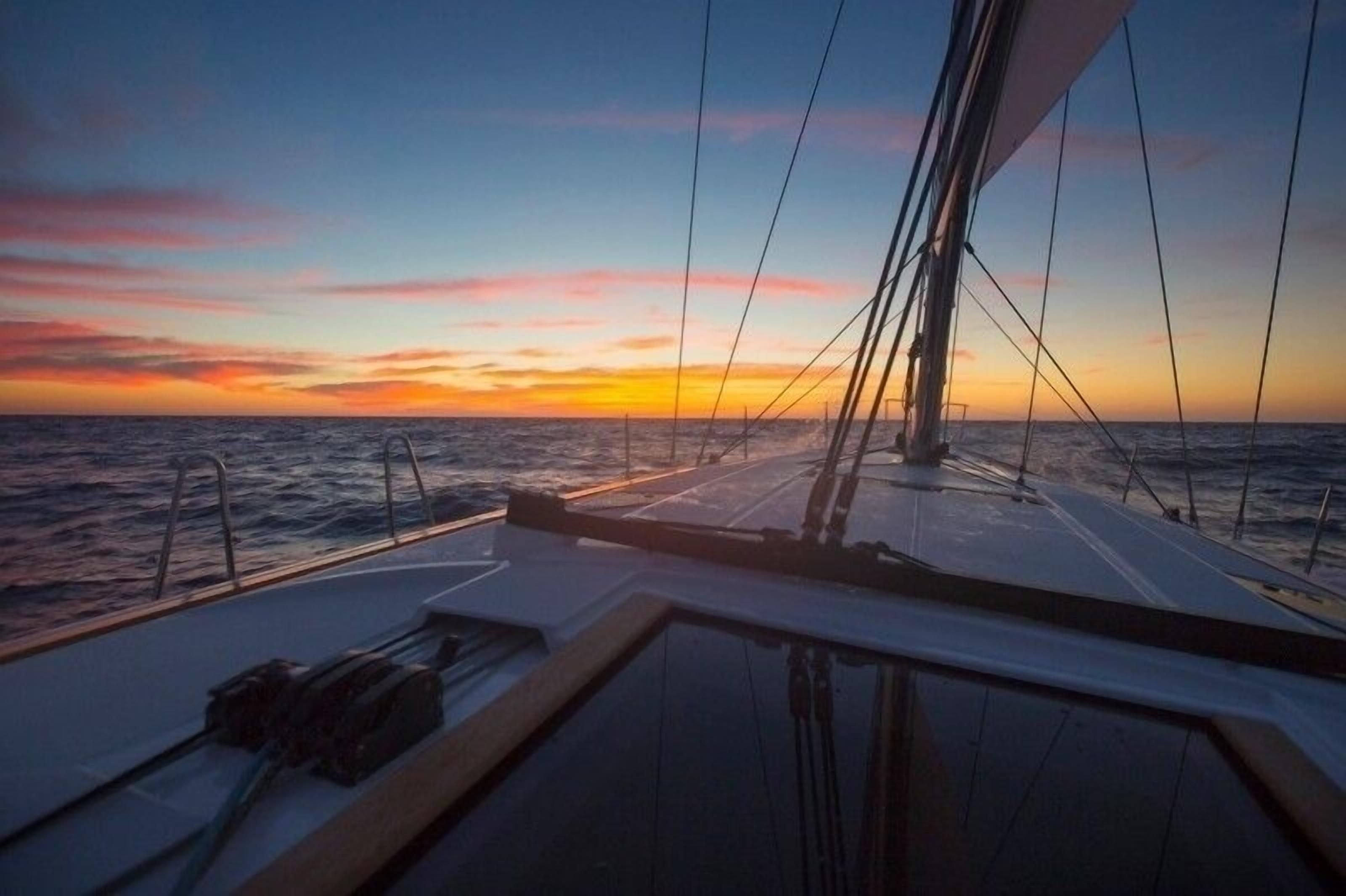 Ein Segelboot auf dem Meer bei Sonnenuntergang mit Blick auf den Horizont.