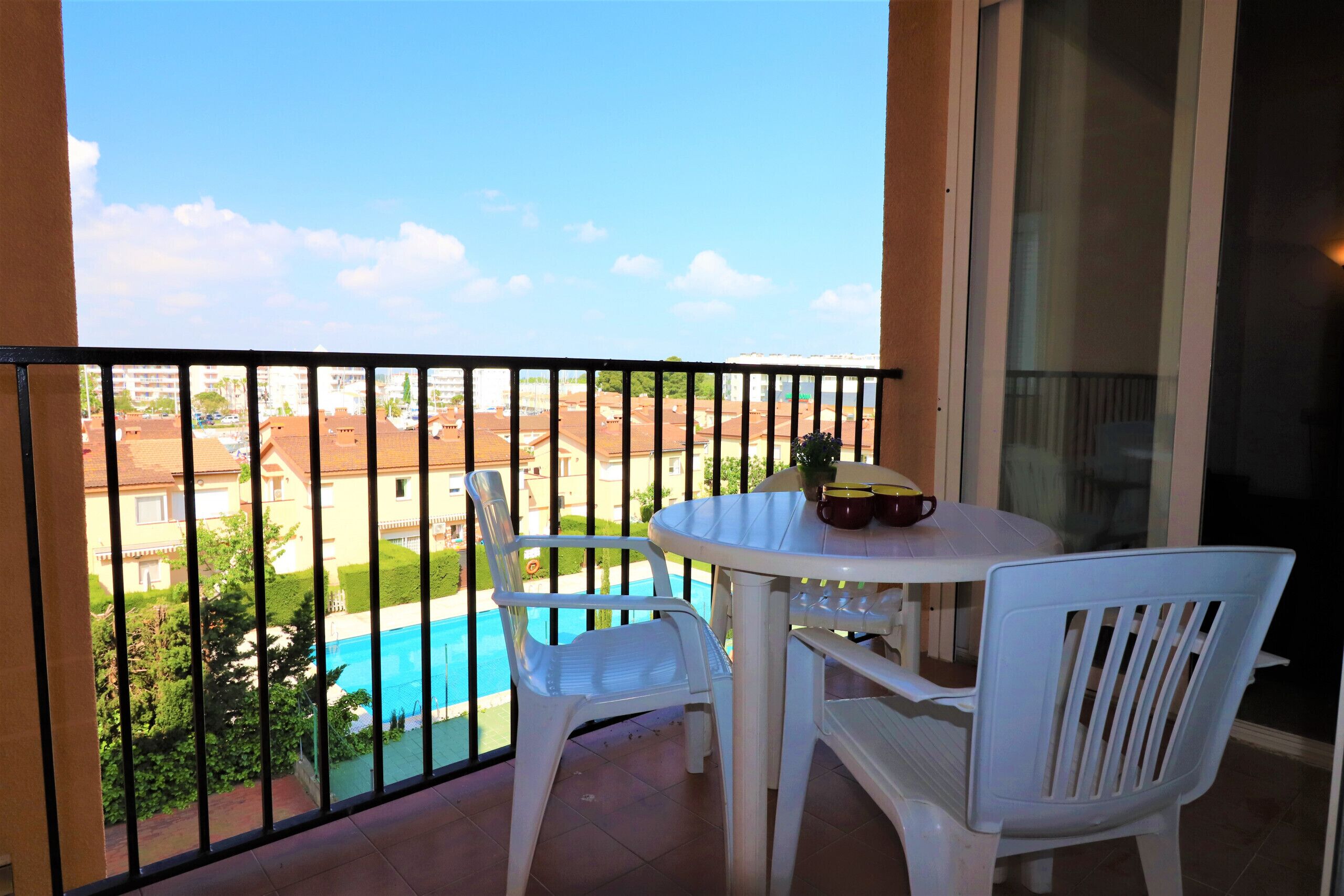 Un balcone con tavolo e sedie, vista su una piscina e un edificio sullo sfondo.