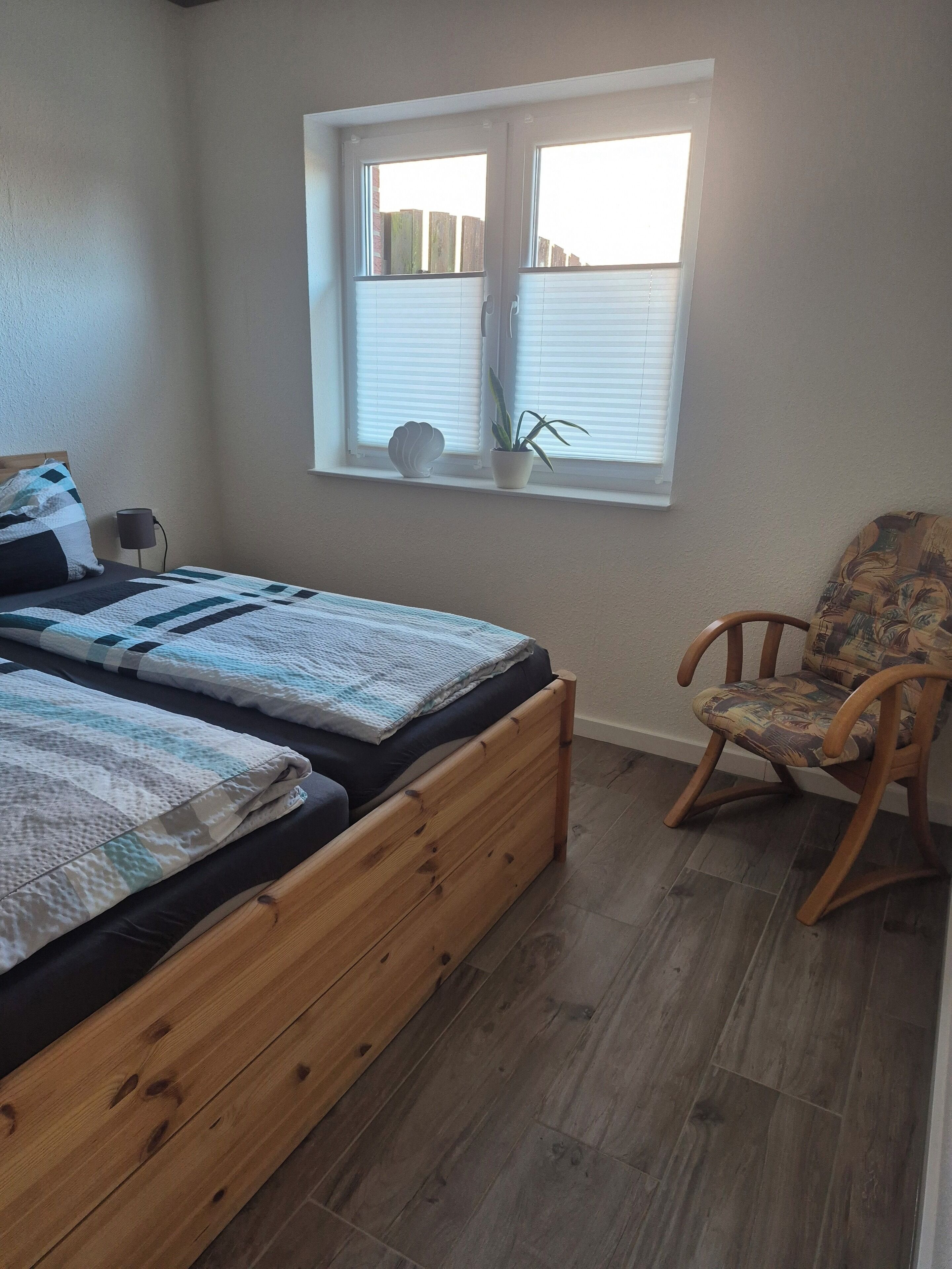 A bedroom with a wooden bed, a chair, a window with blinds, and a potted plant.