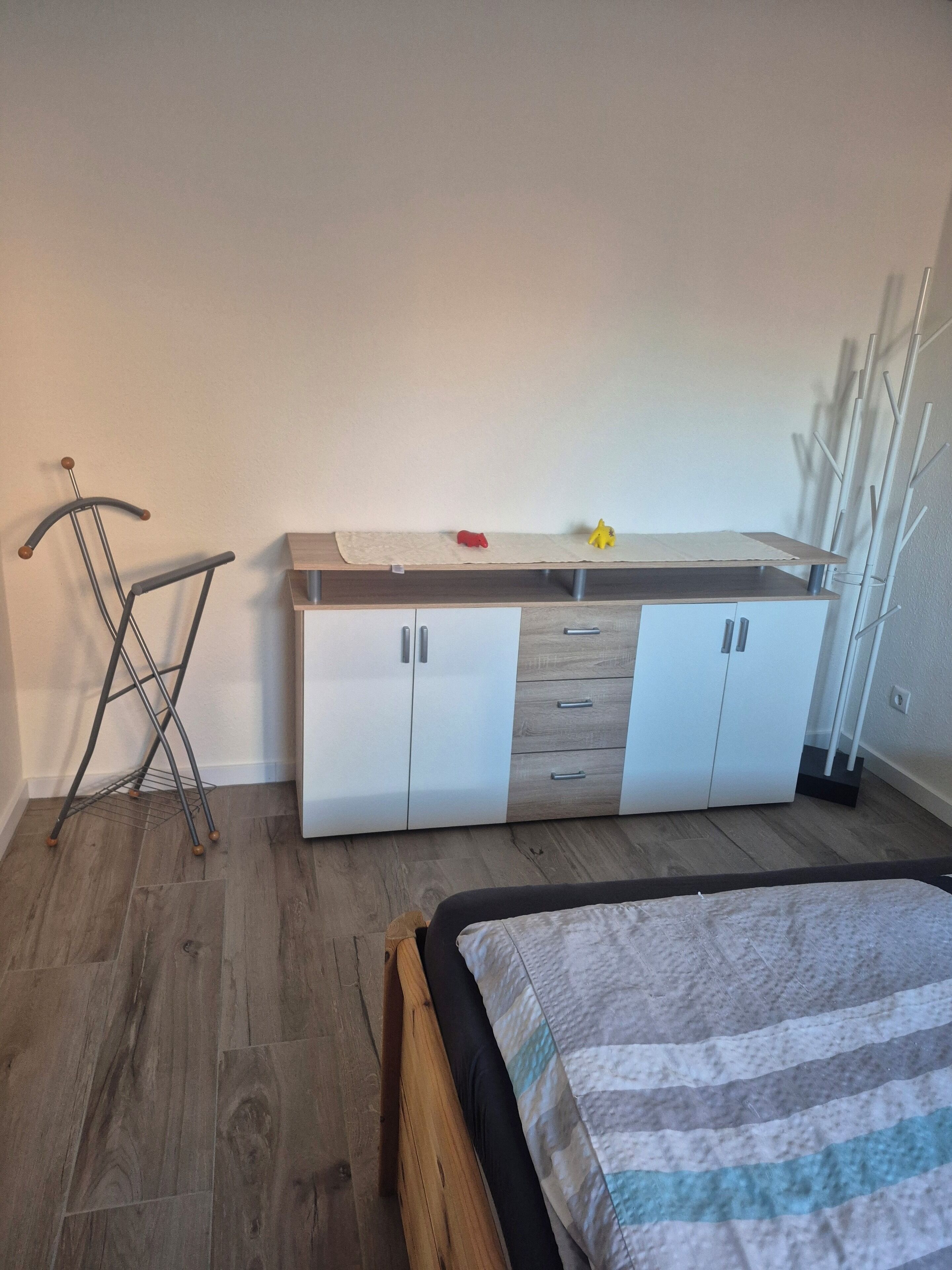 Ein Schlafzimmer mit einem Bett, einem Kleiderschrank, einem Wäscheständer und einem Spiegel.