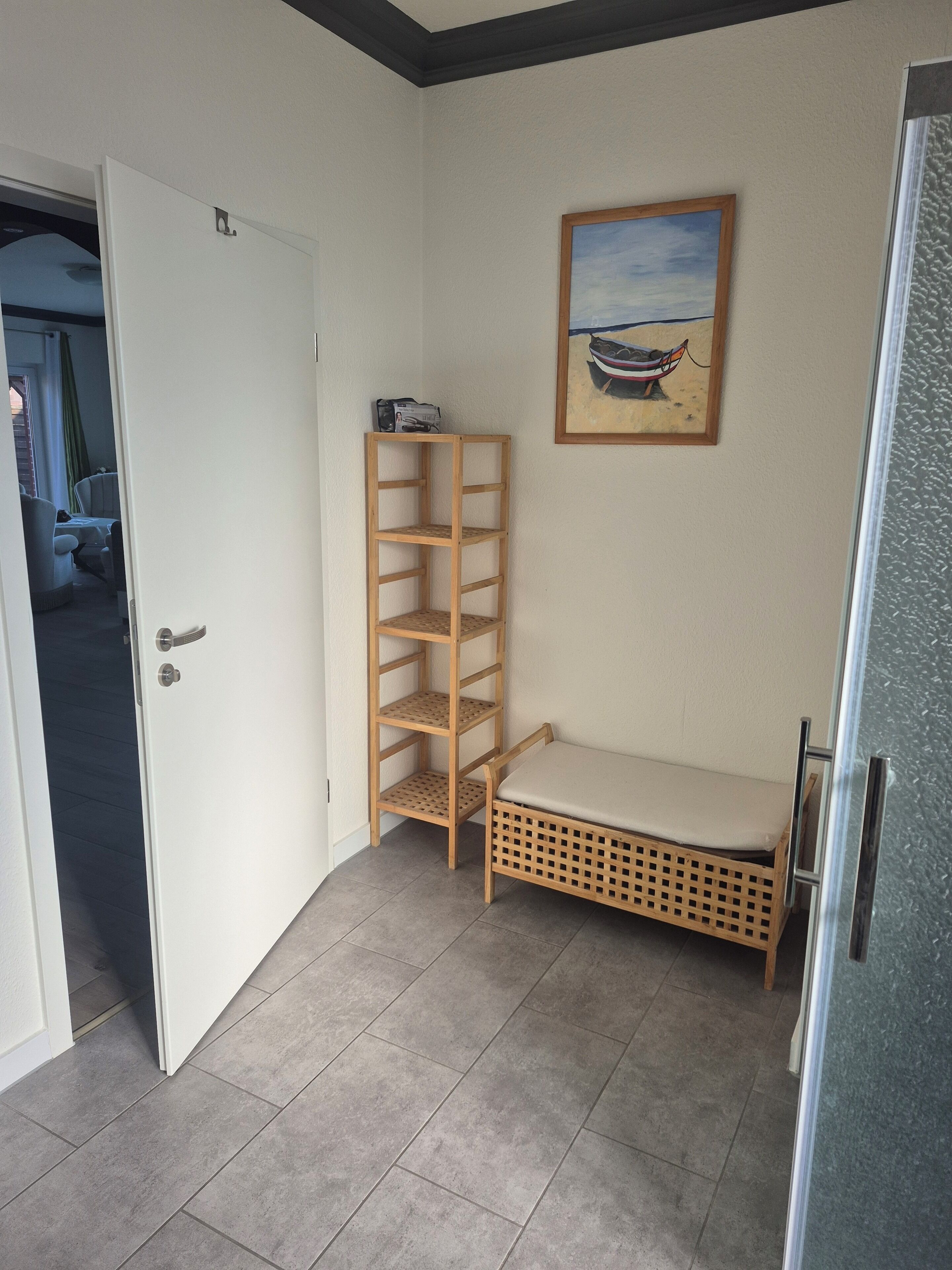 A small room with a white door, a wooden shelf, a bench, and a framed picture on the wall.