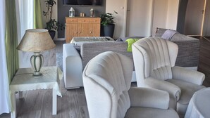 En moderne stue med et fladskærms-tv monteret på væggen, et træskab og et siddeområde med polstrede stole og en sofa.