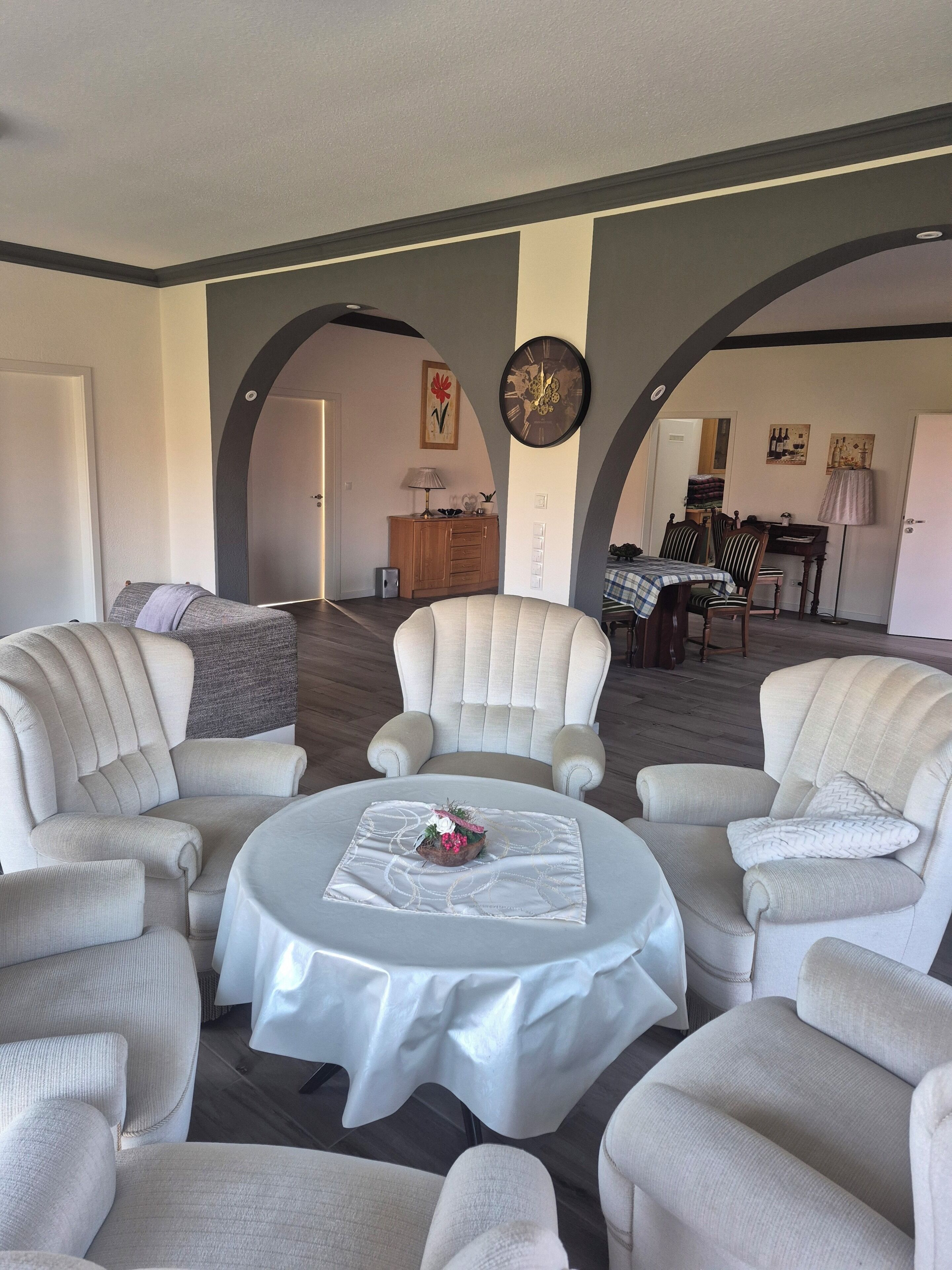 Ein geräumiges Wohnzimmer mit einem runden Tisch, vier Sesseln, einer Holzkabine und einem Essbereich im Hintergrund.