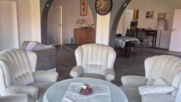 Ein geräumiges Wohnzimmer mit einem runden Tisch, vier Sesseln, einer Holzkabine und einem Essbereich im Hintergrund.