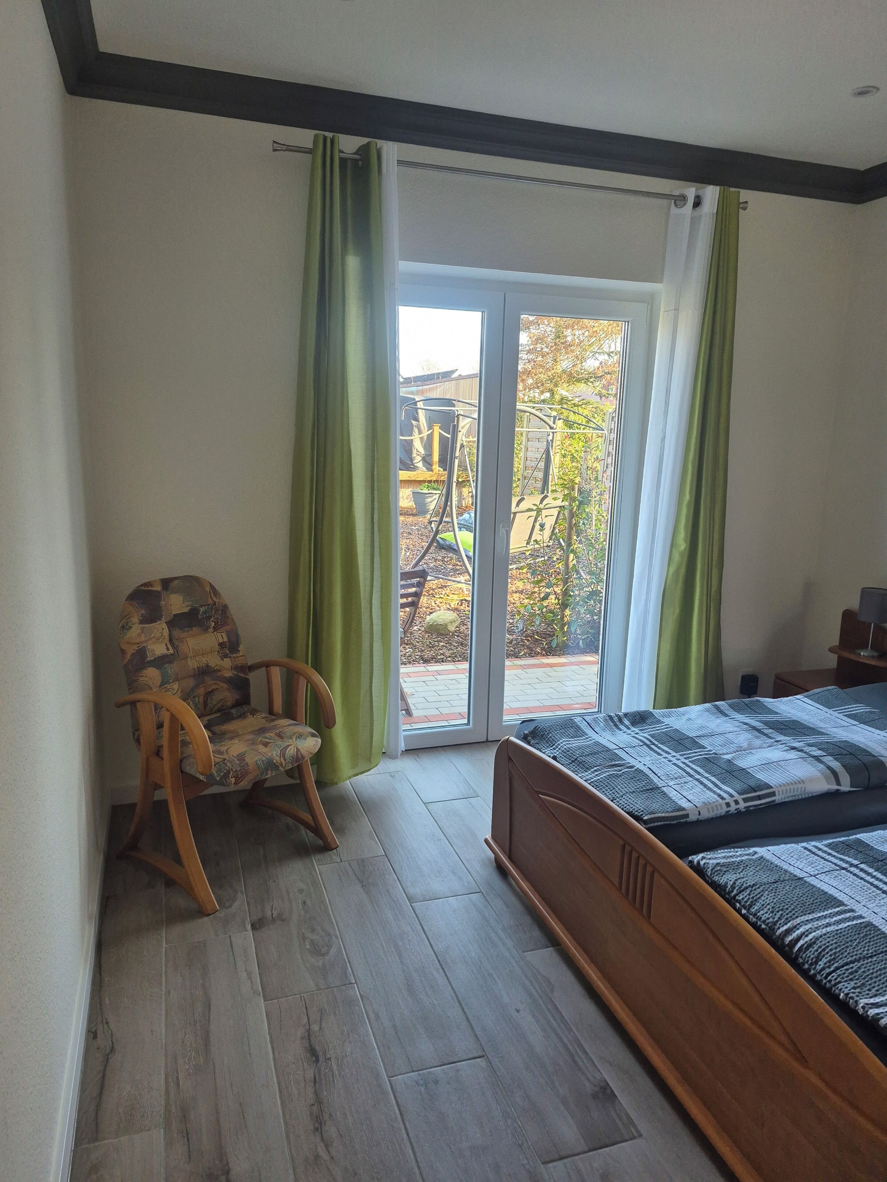 A bedroom with a wooden bed, a rocking chair, and a sliding glass door leading to a garden.