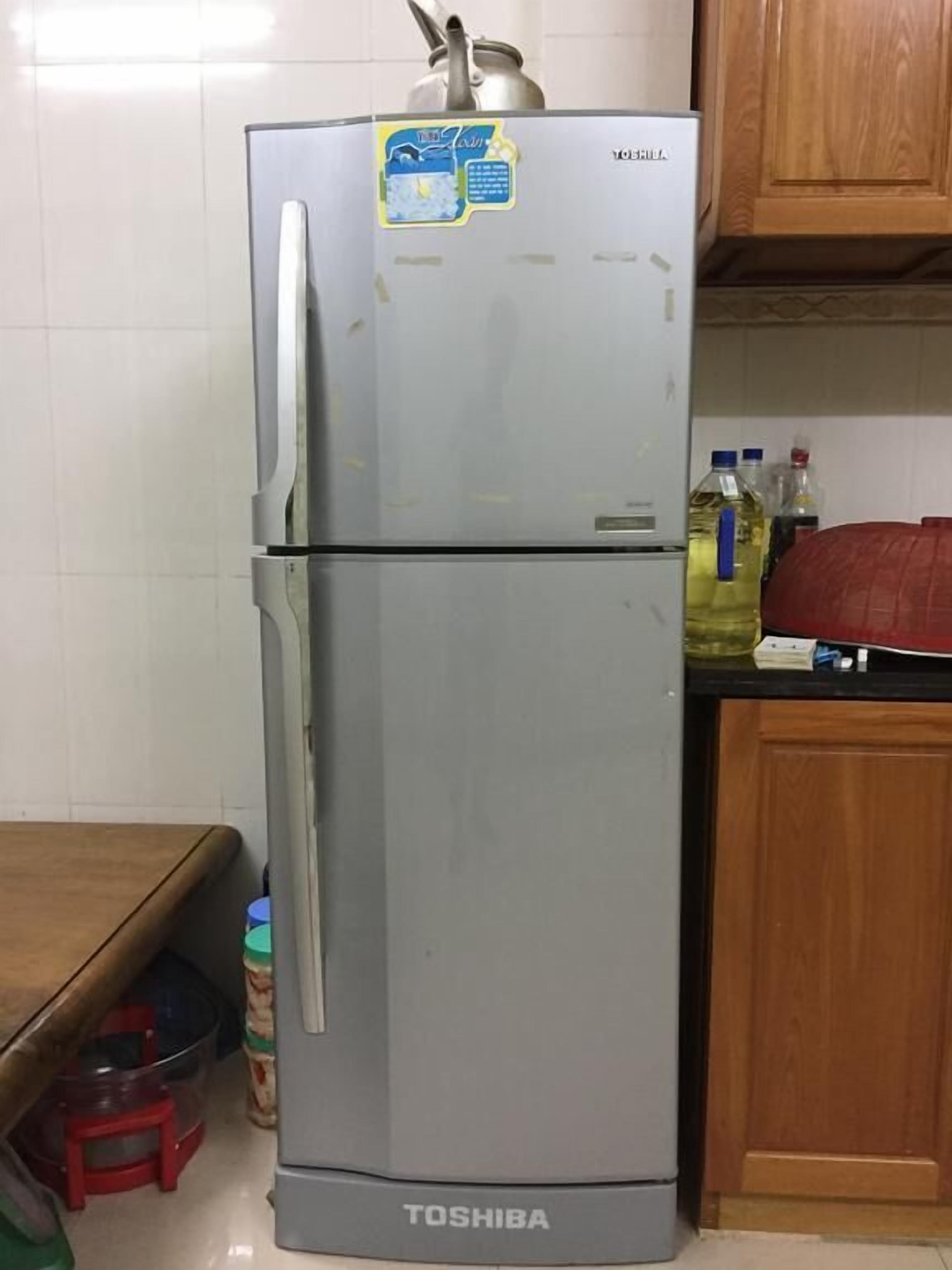 A Toshiba refrigerator in a kitchen with wooden cabinets and a tiled backsplash.