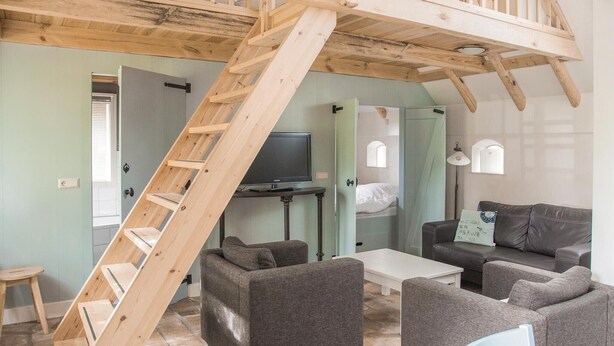 A room with a wooden staircase, grey sofas, a flat-screen TV, and a small table. - Stunning apartment in Wijdenes with house sea view (Wijdenes)