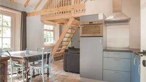 A compact kitchen with a built-in oven, a dining area with a table and chairs, and a loft bedroom with a wooden staircase. - Stunning apartment in Wijdenes with house sea view (Wijdenes)