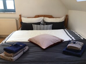 Una cama bien tendida con ropa de cama a rayas, un cabecero de madera y una ventana arriba.