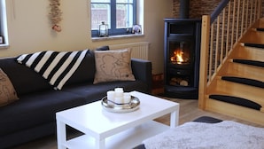 Una sala de estar acogedora con un sofá, una mesa de centro blanca, una chimenea y una escalera de madera.
