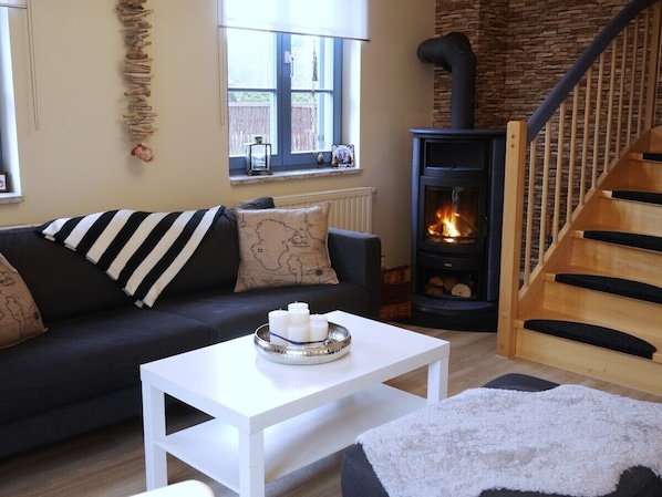 Una sala de estar acogedora con un sofá, una mesa de centro blanca, una chimenea y una escalera de madera.