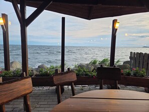 Un área de estar al aire libre con madera y vistas al mar, con un banco y una mesa.