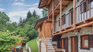 Eine Holzhütte mit Steinmauern, einem Balkon und einer Steintreppe, die zum Eingang führt.
