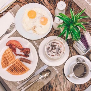 A breakfast setting with eggs, bacon, waffles, and coffee on a wooden table. - Quest Serviced Residences (Cebu City)
