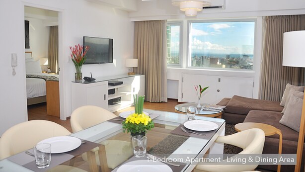 Eine 1-Zimmer-Wohnung mit Essbereich, Wohnzimmer, Fernseher und großem Fenster mit Stadtblick.