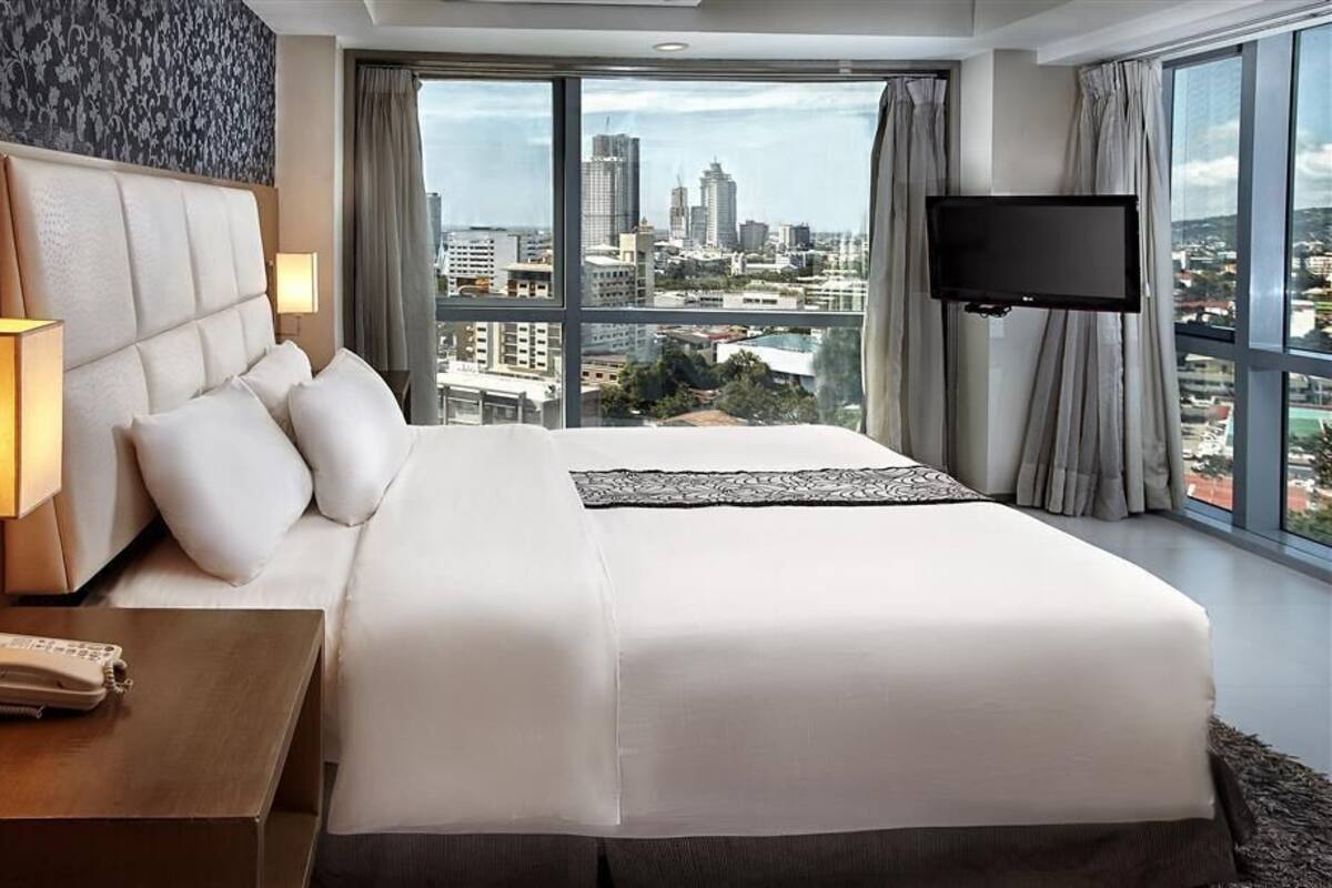 Ein Hotelzimmer mit einem großen Bett, einer Nachttischlampe, einem Telefon und einem Fernseher.