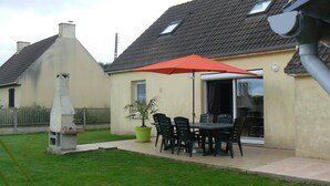 Une maison avec un patio, une cheminée, un pot de fleurs et une table avec des chaises.