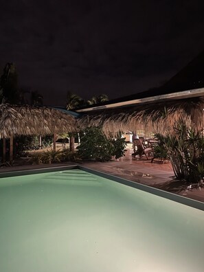 Una piscina con estructuras de techo de paja y asientos exteriores.