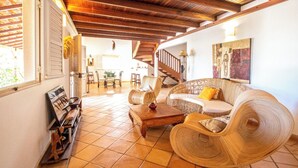 Un espacio habitable amplio con techo de madera, mobiliario de mimbre y una escalera que conduce a otra habitación.
