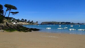 A beach with boats, rocky coastline, and buildings in the background.