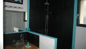 Un bagno moderno con un lavandino a forma di bacinella di vetro, un soffione doccia a mano e un box doccia rivestito di piastrelle nere.