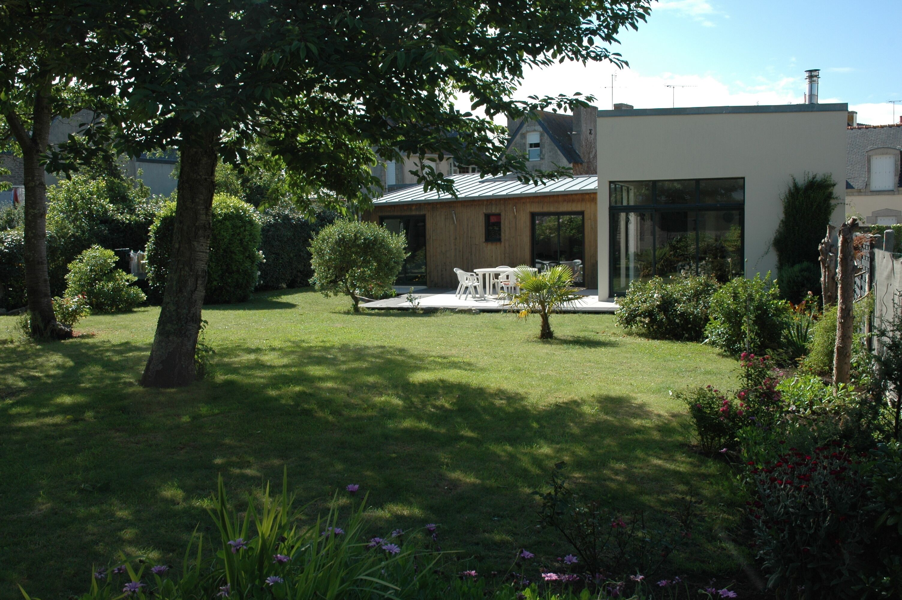 A modern house with a well-maintained garden, a patio with outdoor furniture, and a large window overlooking the garden.