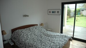 Una camera da letto con un letto, un comodino, una lampada, una sedia e una porta scorrevole in vetro che si apre su un giardino.