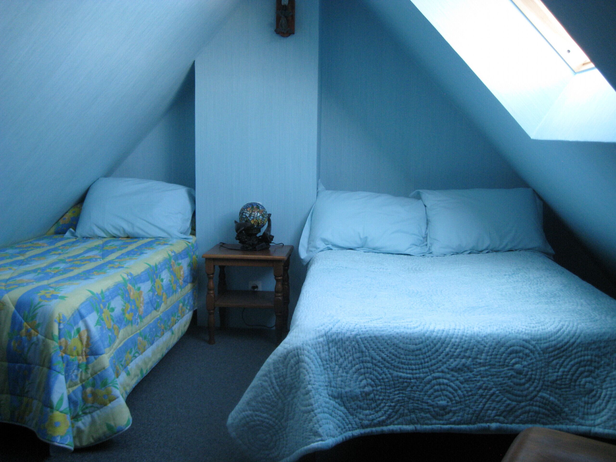 A room with two beds, a small table with a globe, and a skylight.
