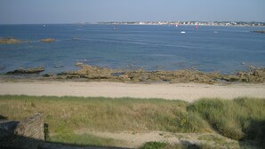 Vista costera con playa de arena, costa rocosa y un pueblo lejano.