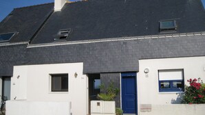 Un edificio de dos plantas con techo oscuro, paredes blancas y puerta azul.