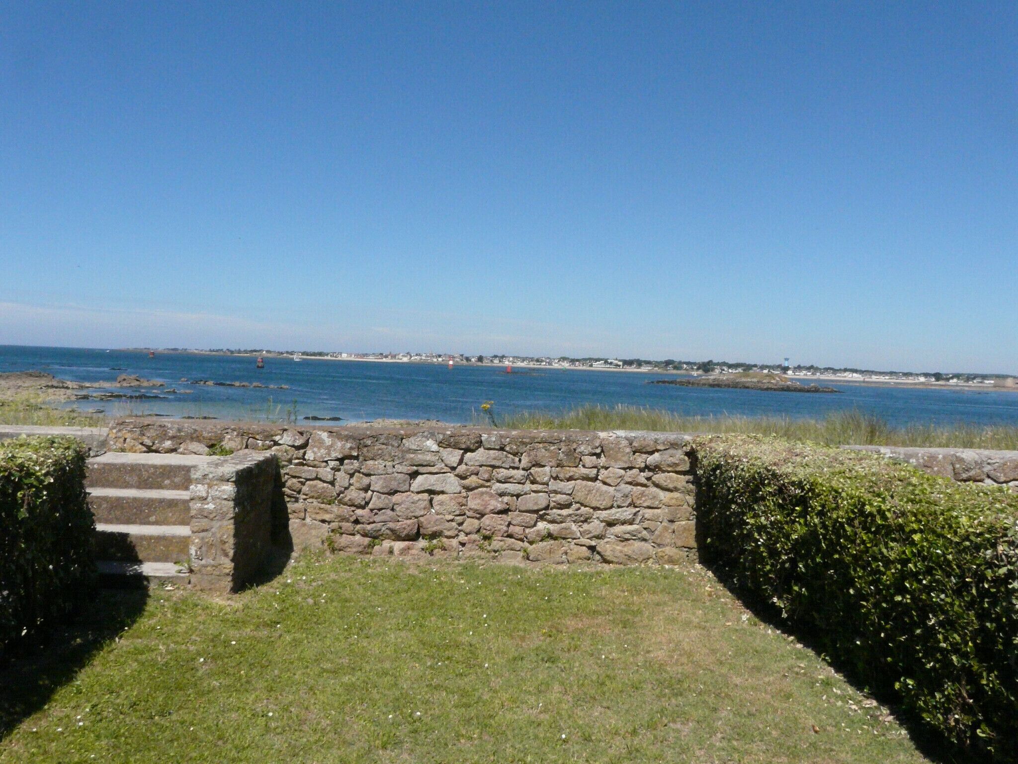 A stone wall leading to a grassy area with a view of the sea and distant shoreline.