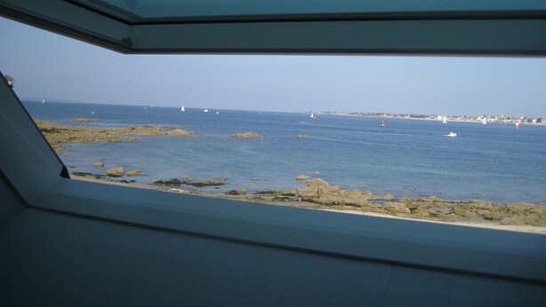 Vista desde el interior de un vehículo hacia una costa rocosa, con el mar y barcos en la distancia.
