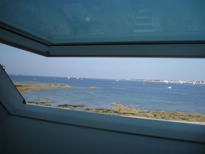 Blick vom Inneren eines Fahrzeugs auf eine felsige Küstenlinie mit Meer und Booten in der Ferne.