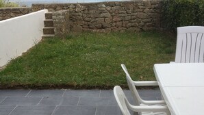 Un patio exterior con muro de piedra, zona con césped y vista al mar.