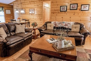 A cozy living room with two leather sofas, a wooden coffee table, and a dining area with a wooden table and chairs. - Deer Tracks Located in Coosawattee Resort (Ellijay)
