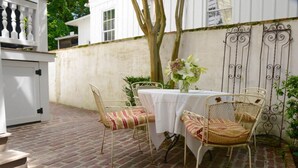 Un patio con suelo de ladrillo, mesa blanca y sillas de mimbre.
